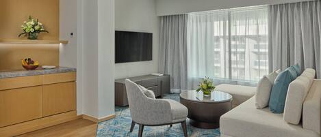 A modern hotel room with a living area, a kitchen, and a large window with curtains.
