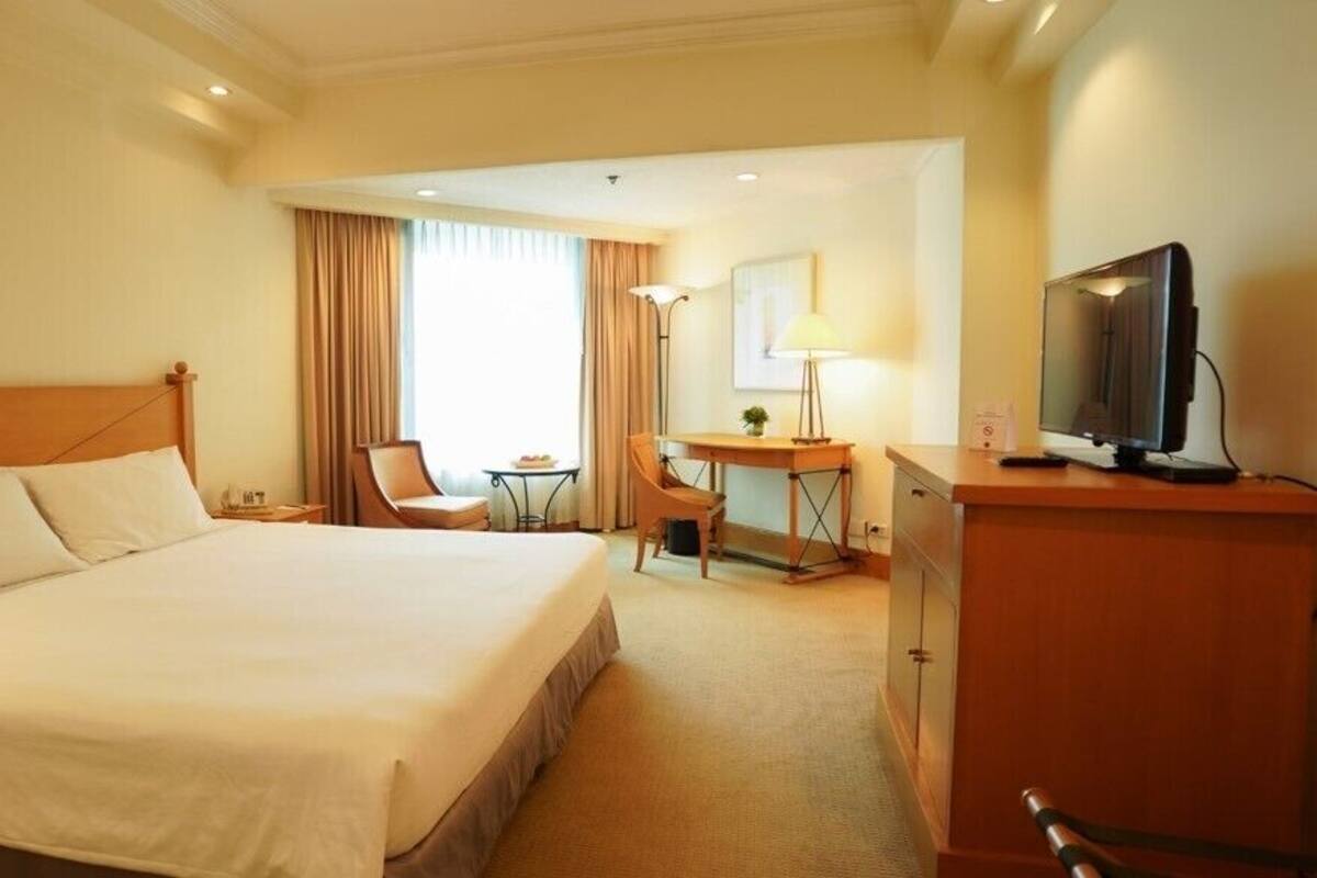 A hotel room with a large bed, a desk with a chair, a television, and a lamp.