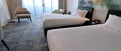 Ein Hotelzimmer mit zwei Betten, einem Sessel, einem Tisch und einem Bild an der Wand.