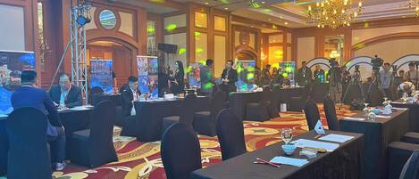 Un salón de conferencias con mesas redondas, sillas y un escenario con un atril.