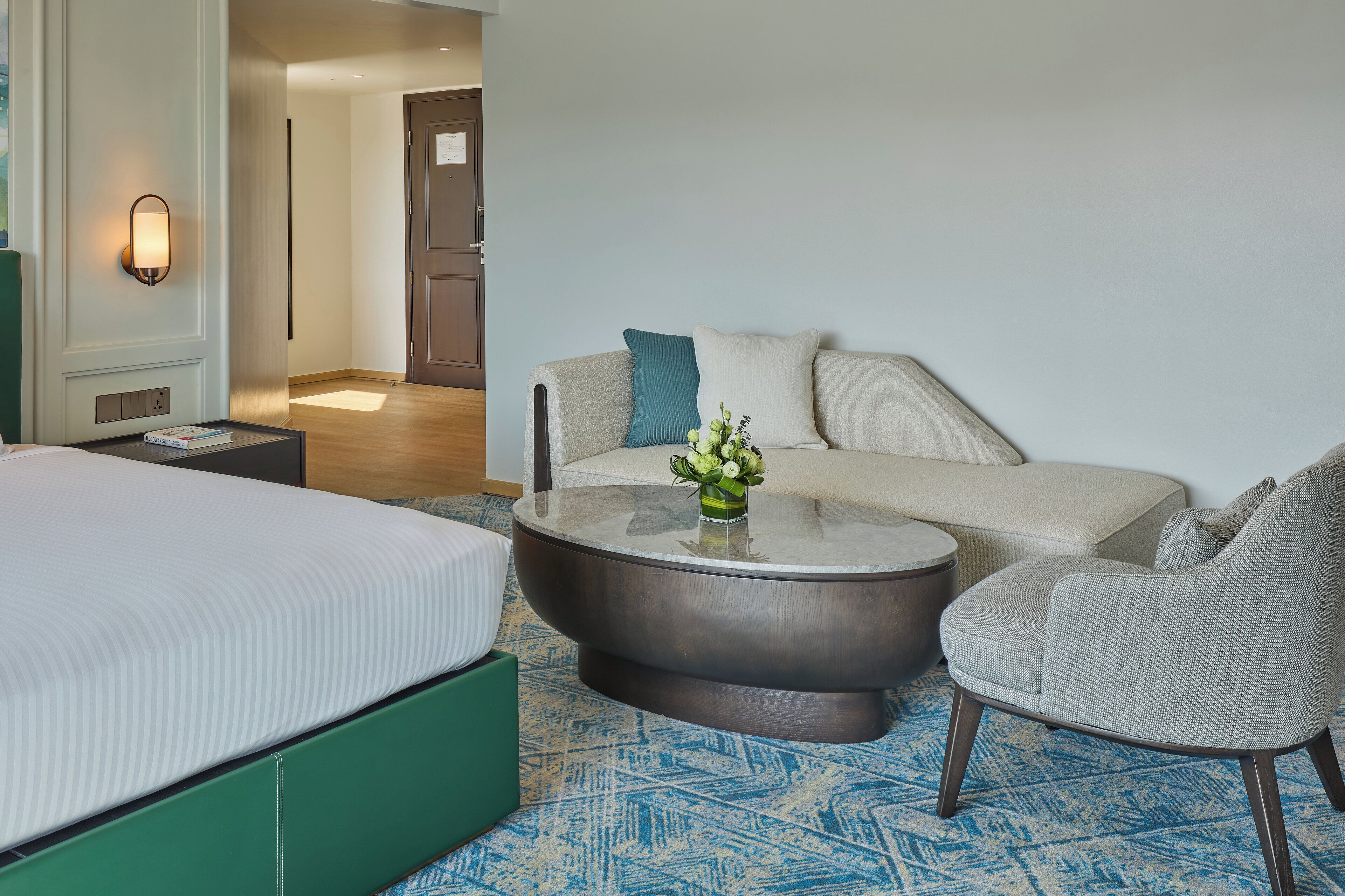 Een hotelkamer met een bed, een ronde salontafel met een vaas, een bank en een stoel.