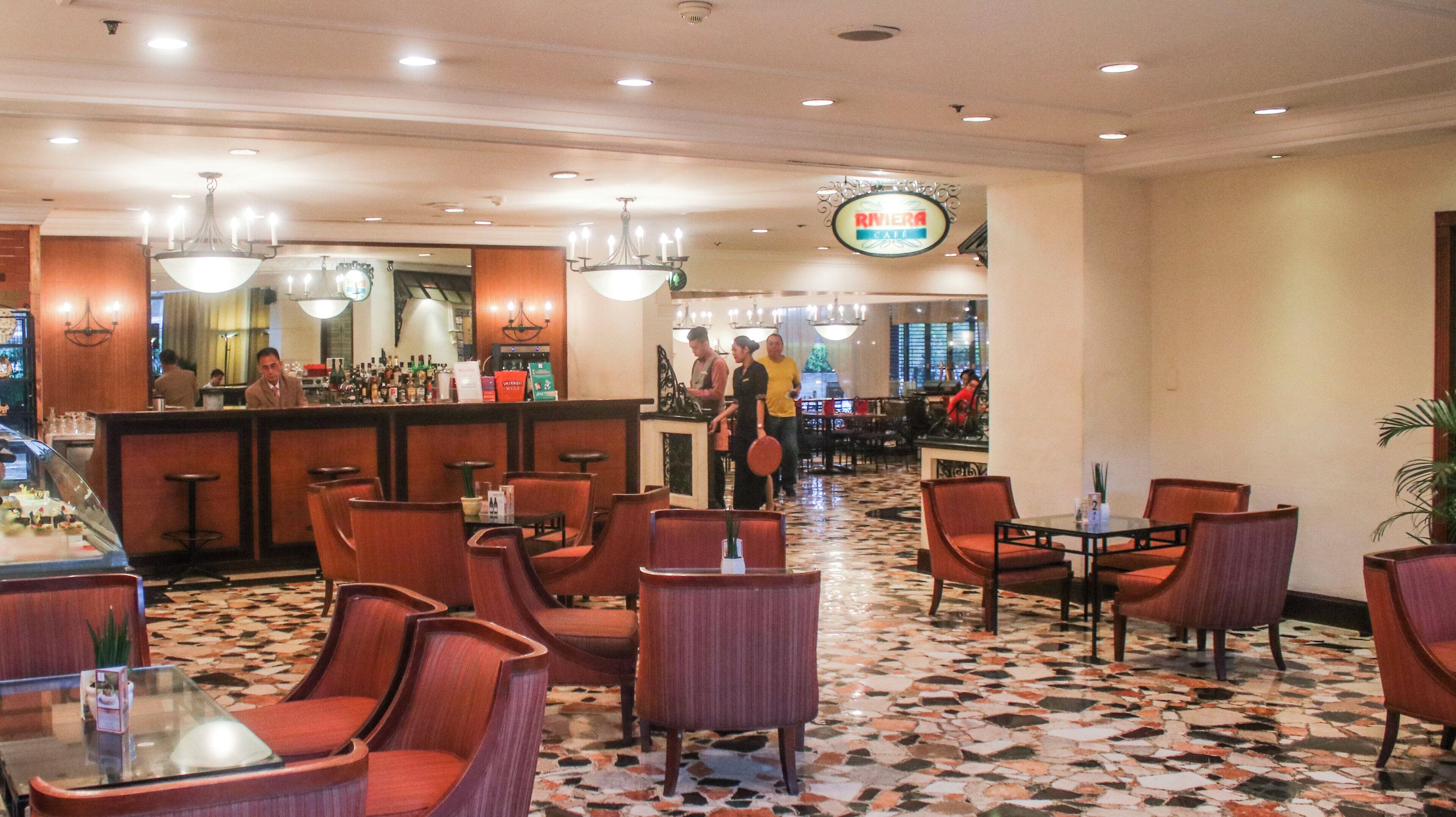 Un vestíbulo de hotel con zona de bar, varios conjuntos de asientos y suelo estampado.