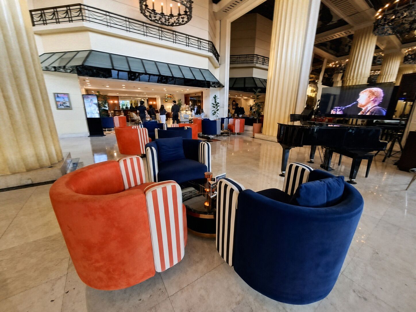 Un'ampia hall con un pianoforte a coda, uno schermo televisivo e un'area relax con poltrone a righe.