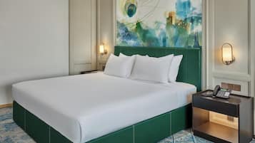 Un lit bien fait, avec du linge de lit blanc, une tête de lit recouverte d’un tissu vert et une table de chevet sur laquelle se trouvent un téléphone et une lampe.