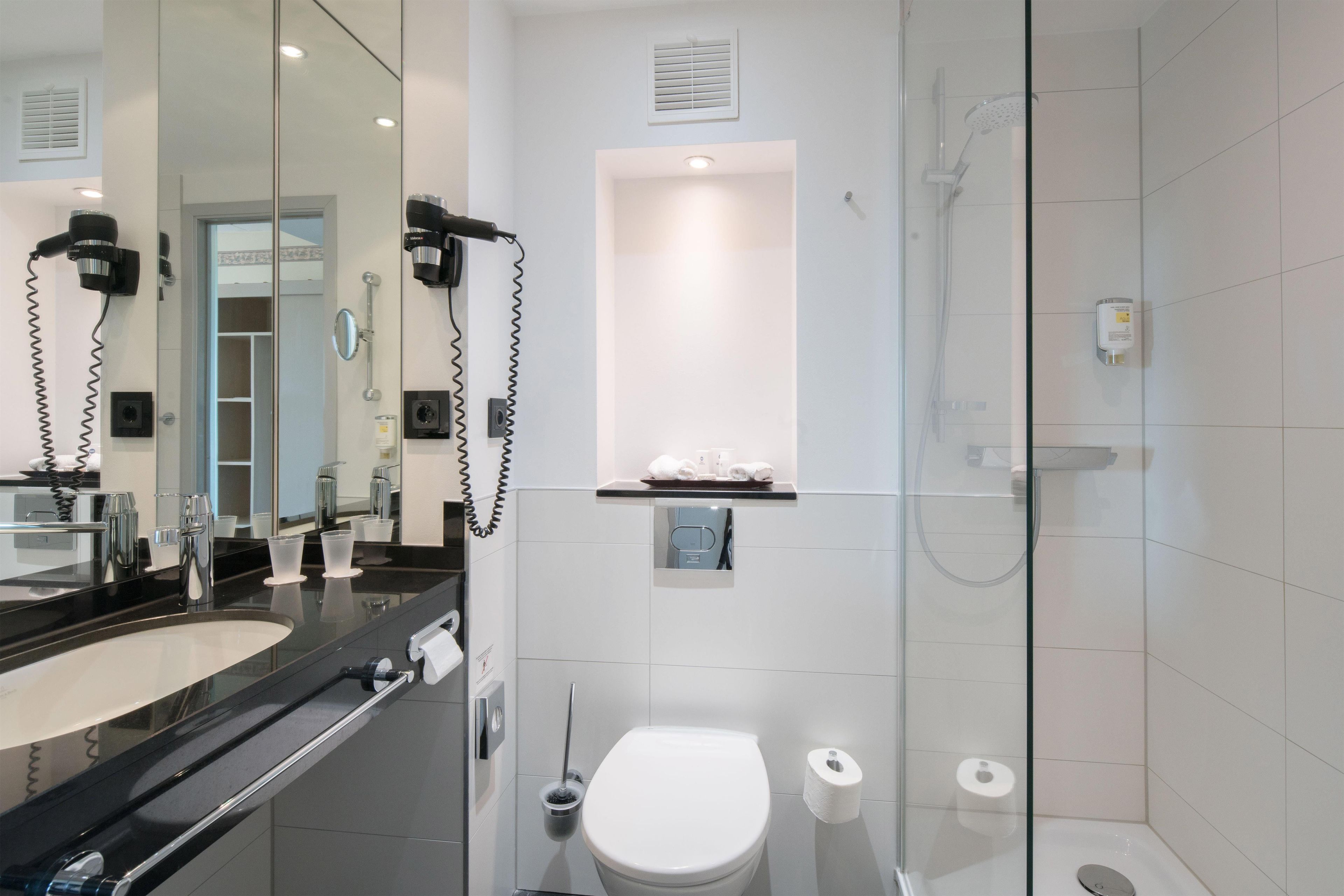 A modern bathroom with a glass shower enclosure, a large mirror, a vanity with a black countertop, and a toilet.
