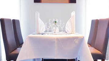 Une table à manger recouverte d’une nappe blanche, entourée de quatre chaises, dans une pièce où un tableau est accroché au mur.