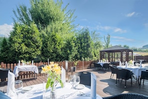 Een terras met tafels gedekt voor een maaltijd, omringd door groen en een houten omheining.