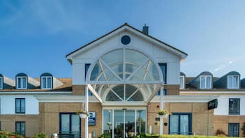 A hotel with a central glass facade, a brick facade, and a clear blue sky.