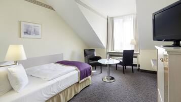 Habitación de hotel con cama, escritorio, silla, televisor y ventana con cortinas.