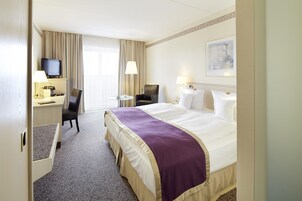 Una habitación de hotel con cama, escritorio, silla, televisor y un cuadro en la pared.