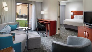 A hotel room with a bed, a desk, a sofa, a TV, and a view of the outdoor area. - Courtyard by Marriott Fayetteville (Fayetteville)