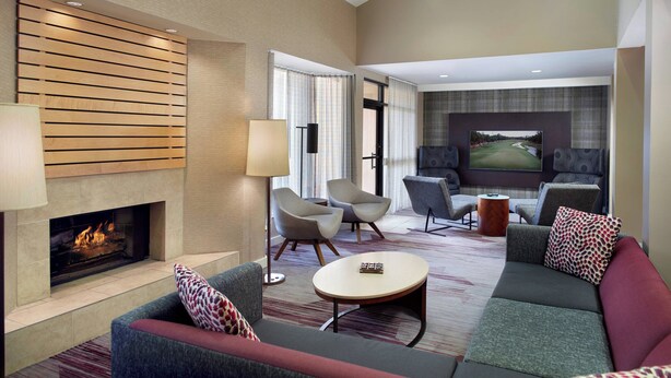 A modern hotel room with a fireplace, comfortable seating, and a large TV screen. - Courtyard by Marriott Fayetteville (Fayetteville)