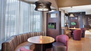 A modern hotel lobby with a round wooden table, cushioned seating, and a television mounted on the wall. - Courtyard by Marriott Fayetteville (Fayetteville)
