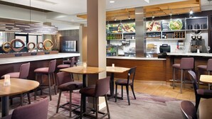 A modern restaurant with round tables, cushioned chairs, and a bar area with food displays and beverage dispensers. - Courtyard by Marriott Fayetteville (Fayetteville)