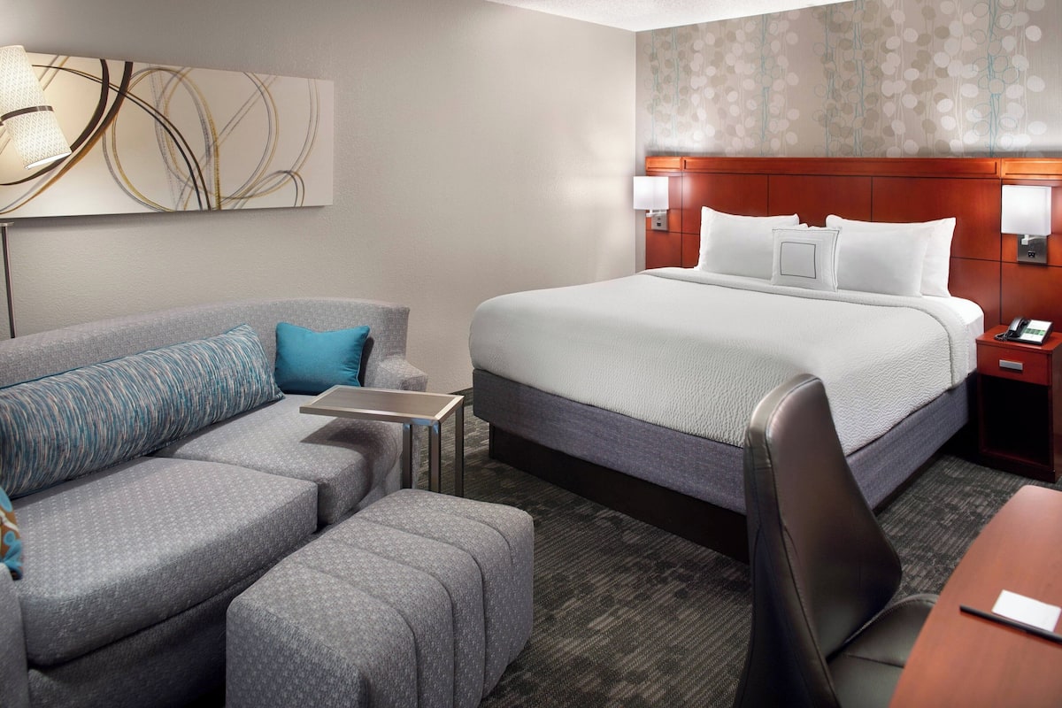 Een hotelkamer met een groot bed, een grijze bank, een klein tafeltje en een bureau.