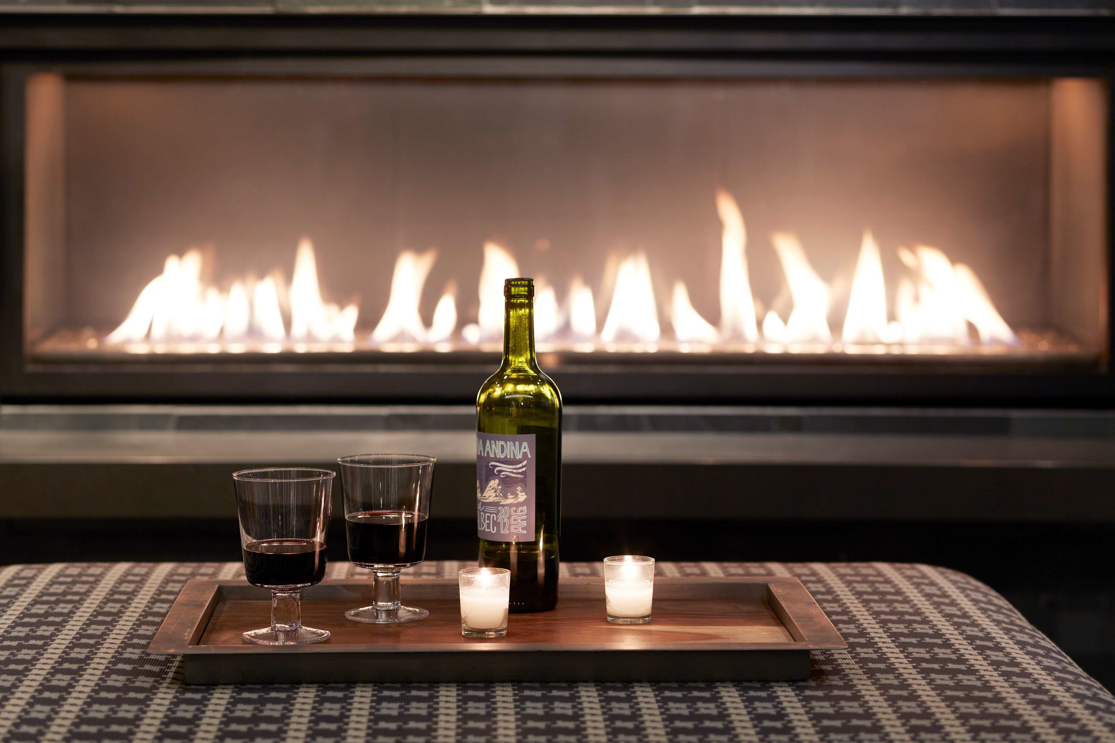 A fireplace with a bottle of wine and glasses on a tray.