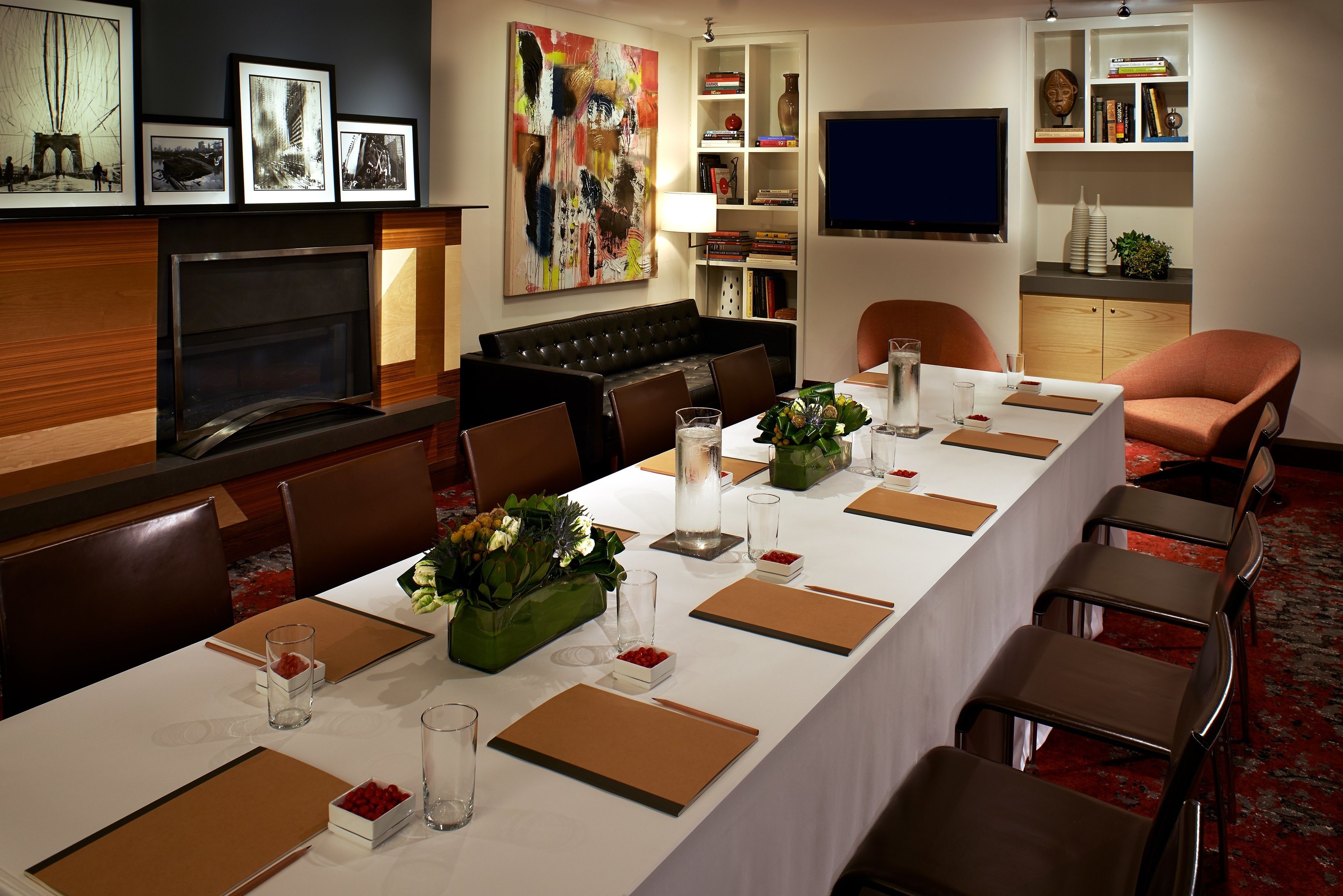 Un salón de conferencias con una larga mesa dispuesta para reuniones, una chimenea y un televisor en la pared.