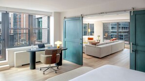 Quarto de hotel moderno com uma cama grande, uma escrivaninha com um laptop, um sofá e uma varanda com vista para a cidade.