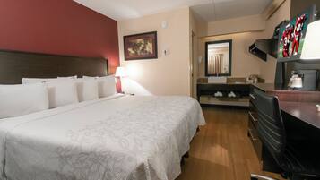 A hotel room with a large bed, a desk with a chair, a mirror, and a television.