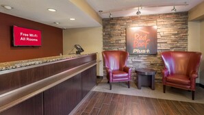 Un espace d’accueil avec un panneau rouge indiquant que le Wi-Fi est gratuit, un mur en pierre orné d’un panneau « Red Roof Plus », et deux fauteuils en cuir.
