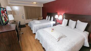 Een hotelkamer met twee bedden, een bureau, een televisie en een rode muur.