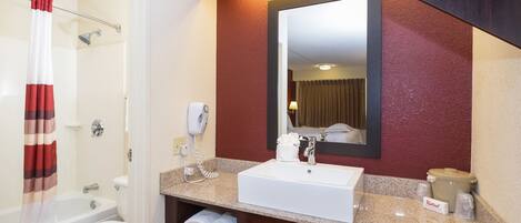 A hotel bathroom with a white sink, a mirror, a towel rack, and a shower curtain.