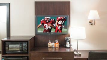 A hotel room with a television mounted on a wooden cabinet, a desk with a lamp, and a chair.