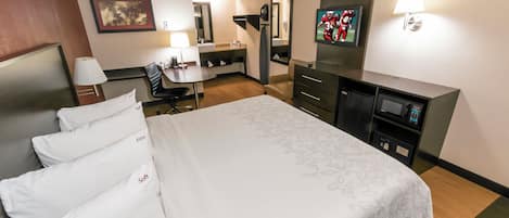 Una habitación de hotel con una cama grande, un escritorio, una silla, un televisor, un espejo y un microondas.