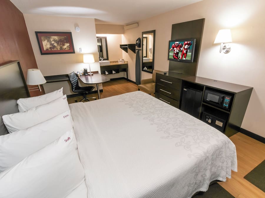 Quarto de hotel com cama grande, escrivaninha, cadeira, televisão, espelho e micro-ondas.