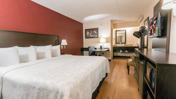A hotel room with a large bed, a desk, a chair, a television, and a minibar.