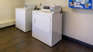 A laundry area with two white washing machines and a wall-mounted sign advertising cleaning products. - Red Roof Inn PLUS+ Columbus - Dublin  (Dublin)