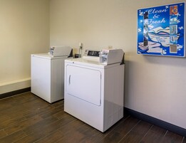 Een wasserette met twee witte wasmachines en een bord aan de muur waarop schoonmaakproducten worden aangeboden.