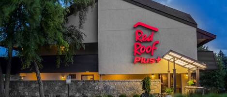 A Red Roof Plus hotel with a modern facade, stone wall, and a parking lot.