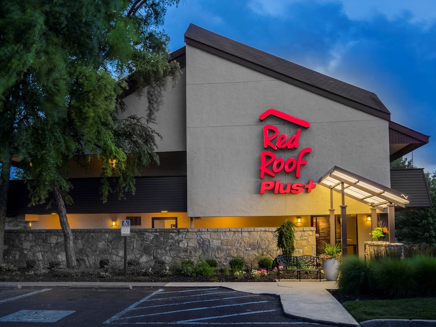 Un hotel Red Roof Plus con una fachada moderna, pared de piedra y un estacionamiento.