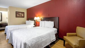 Une chambre d’hôtel avec deux lits, une chaise, une lampe et un tableau au mur.