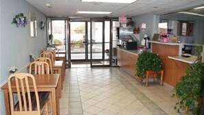 A restaurant with a tiled floor, wooden tables and chairs, a counter with a cash register, and potted plants. - Boise Inn (Boise)