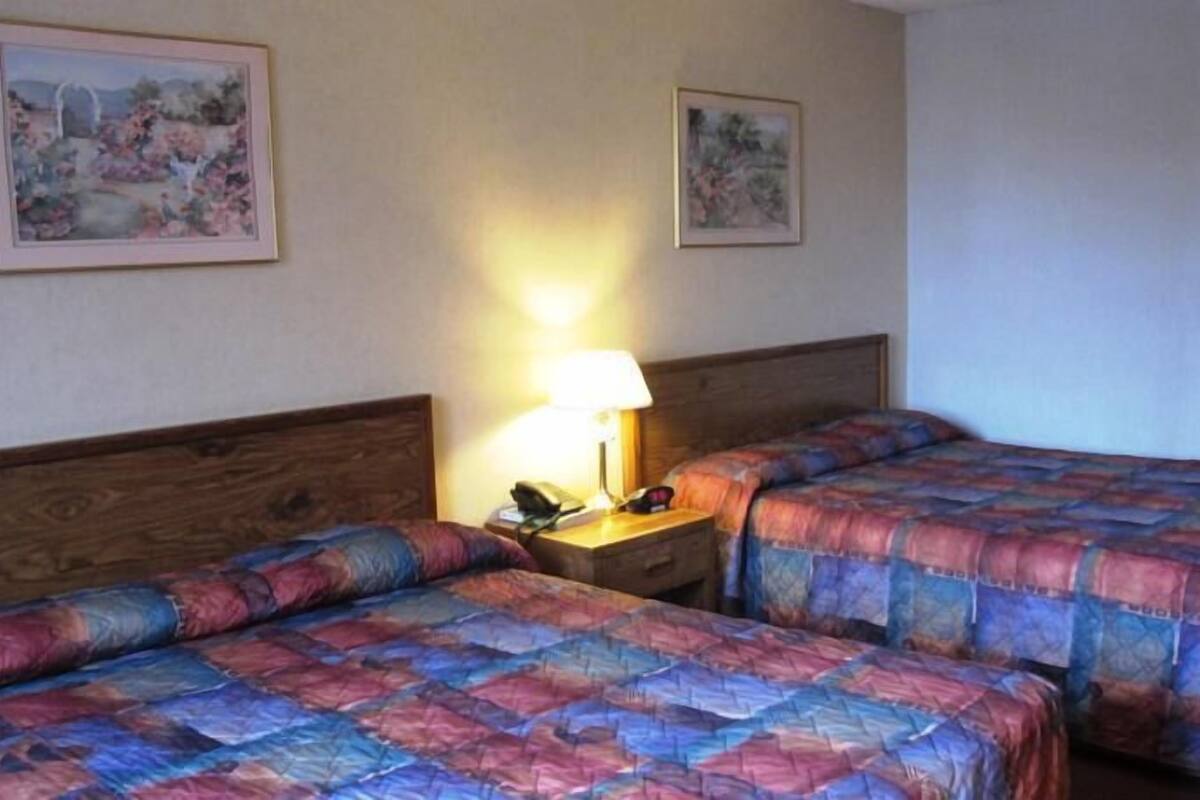 A hotel room with two beds, a nightstand with a lamp, and two framed pictures on the wall.