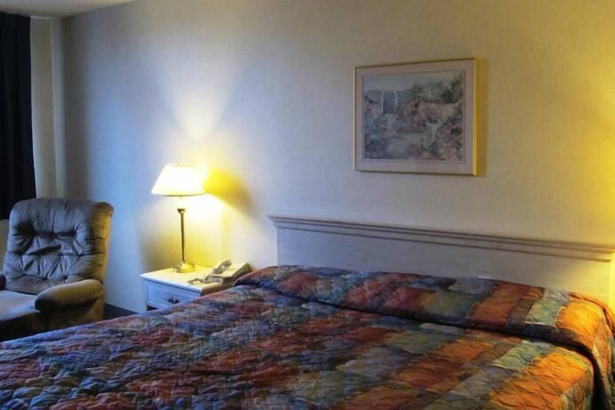 A hotel room with a bed, a chair, two bedside tables with lamps, and a painting on the wall.