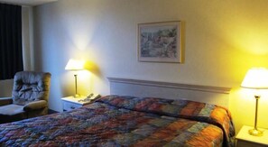 A hotel room with a bed, a chair, two bedside tables with lamps, and a painting on the wall.