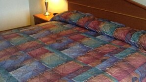 A bed with a colorful quilt, a wooden headboard, and a nightstand with a lamp. - Boise Inn (Boise)