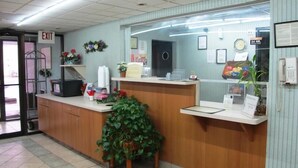 A reception desk with a computer, a telephone, and a plant. There is an exit sign on the wall and a clock. - Boise Inn (Boise)