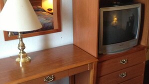 A wooden bedside table with a lamp, a television on a wooden cabinet, and a mirror on the wall. - Boise Inn (Boise)