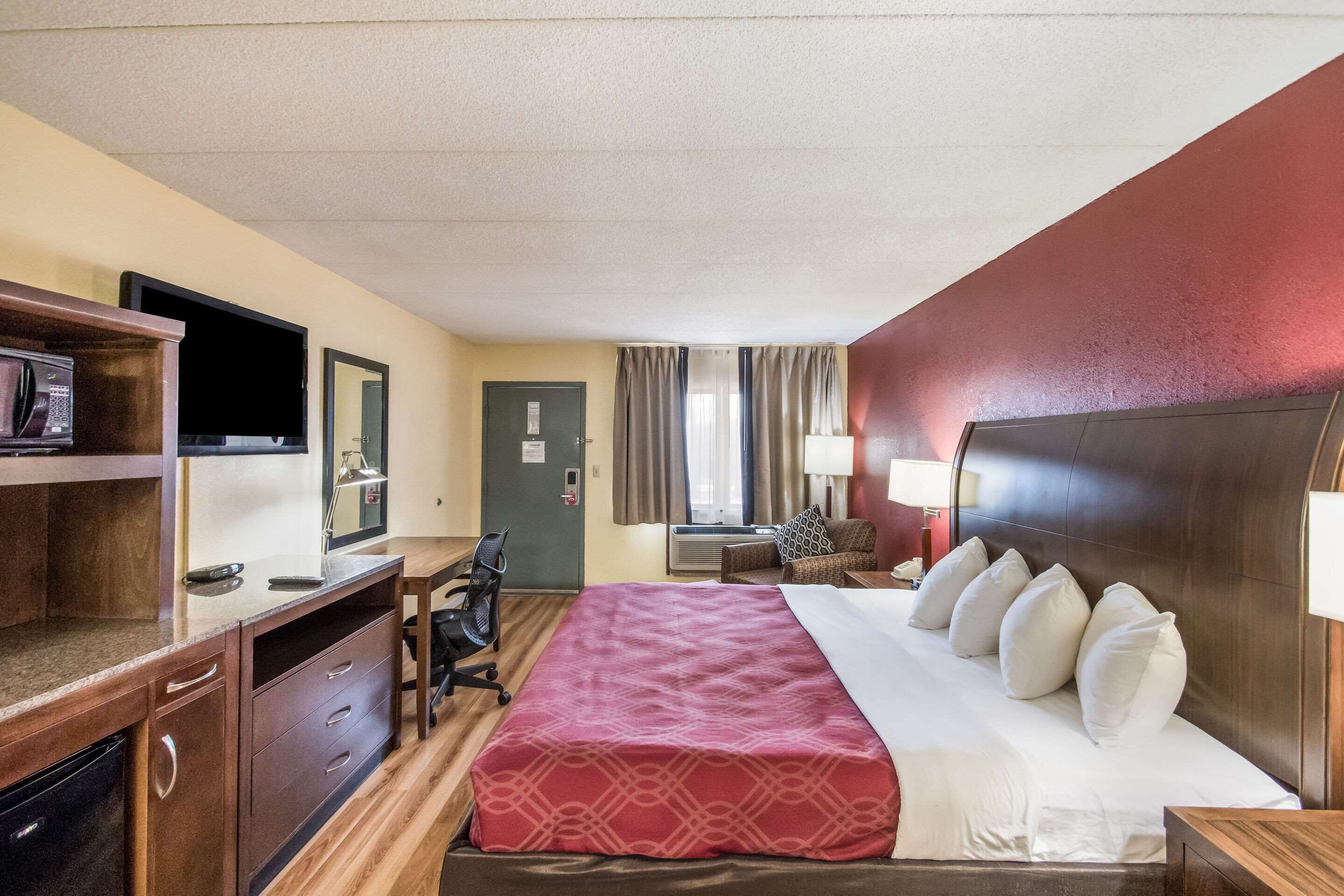 A hotel room with a bed, a desk, a chair, a microwave, a television, and a window with curtains.