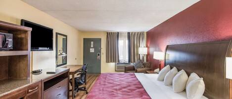 A hotel room with a bed, a desk, a chair, a microwave, a television, and a window with curtains.