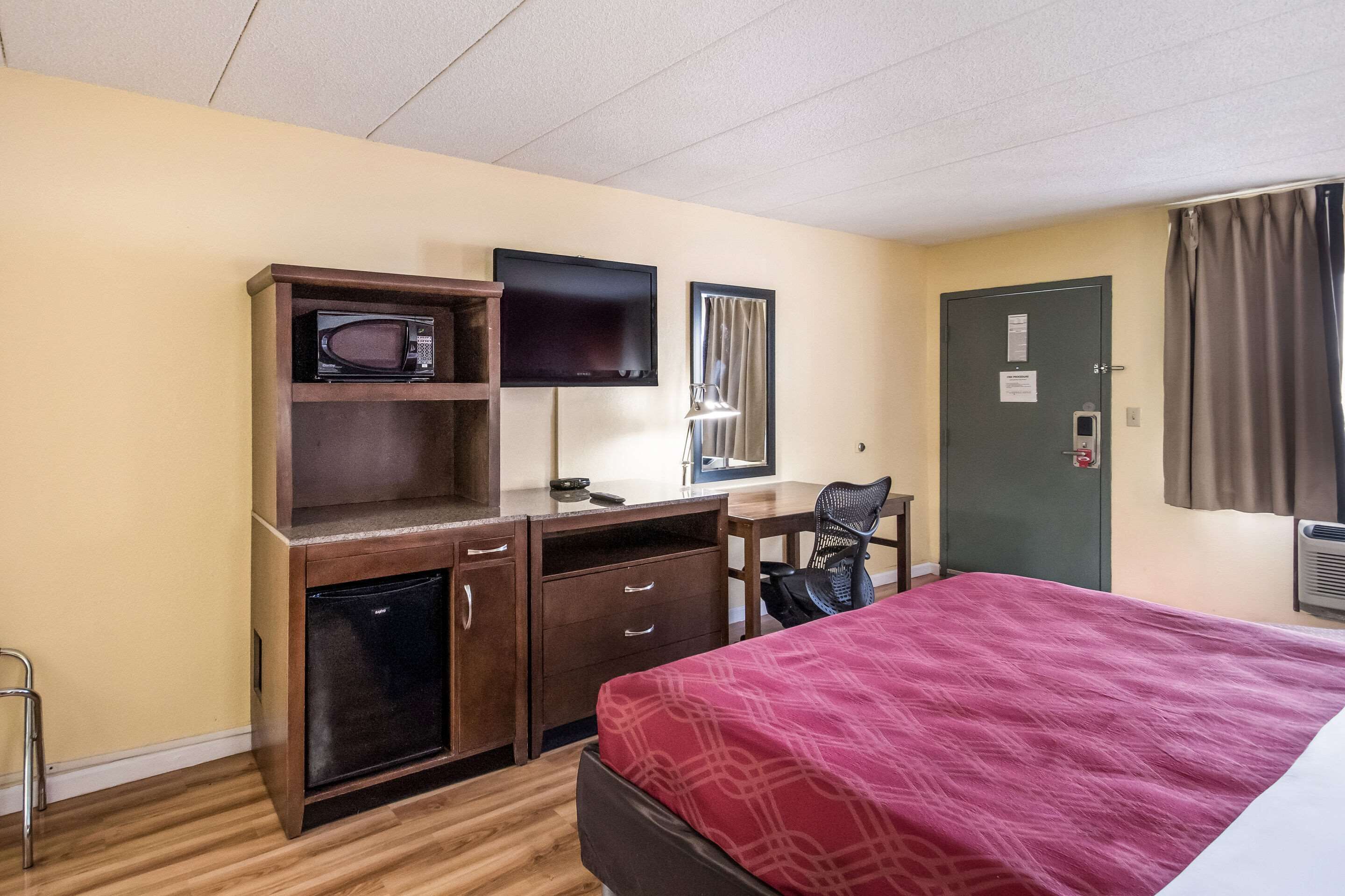 Een hotelkamer met een bed, een bureau met stoel, een magnetron, een televisie en een kledingkast.