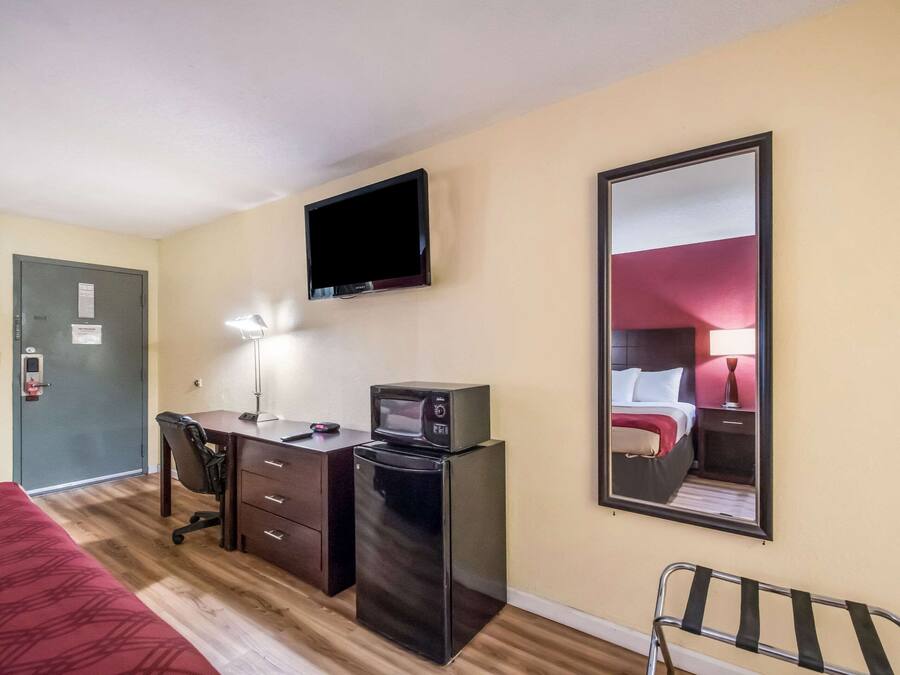 Habitación de hotel con cama, escritorio con computadora, microondas, refrigerador, televisión y espejo.