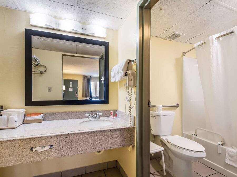 A hotel bathroom with a sink, mirror, towel rack, and a shower area.