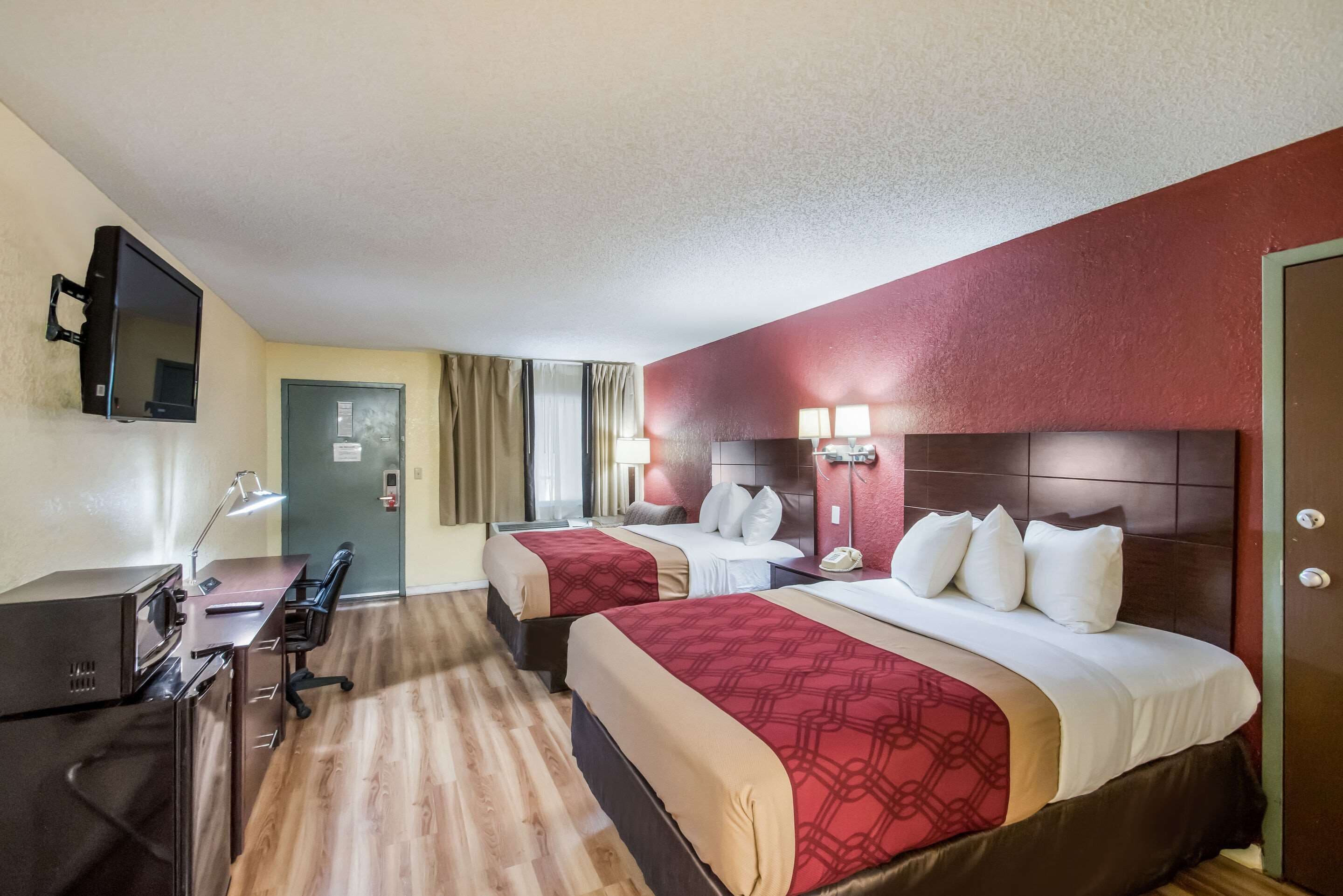 Camera d'albergo con due letti, una scrivania con computer, televisione e lampada da tavolo.