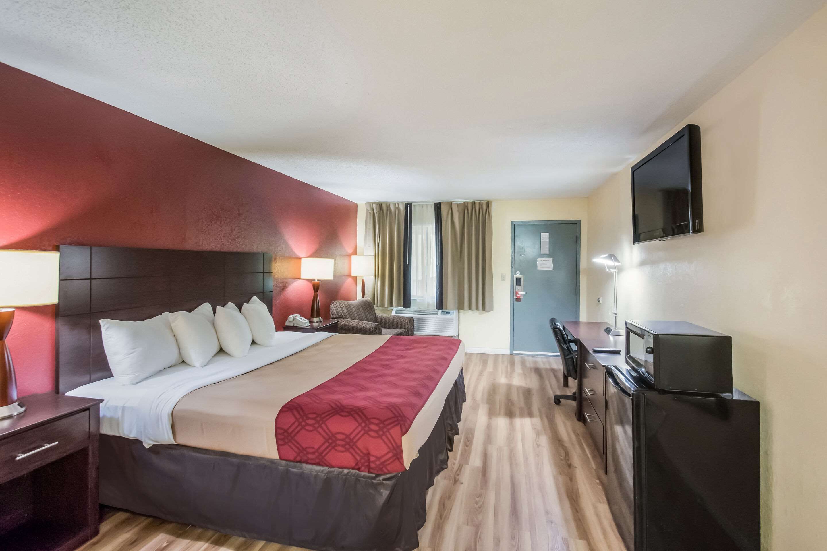 Een hotelkamer met een bed, nachtkastje, lamp, televisie, bureau en een koelkast.