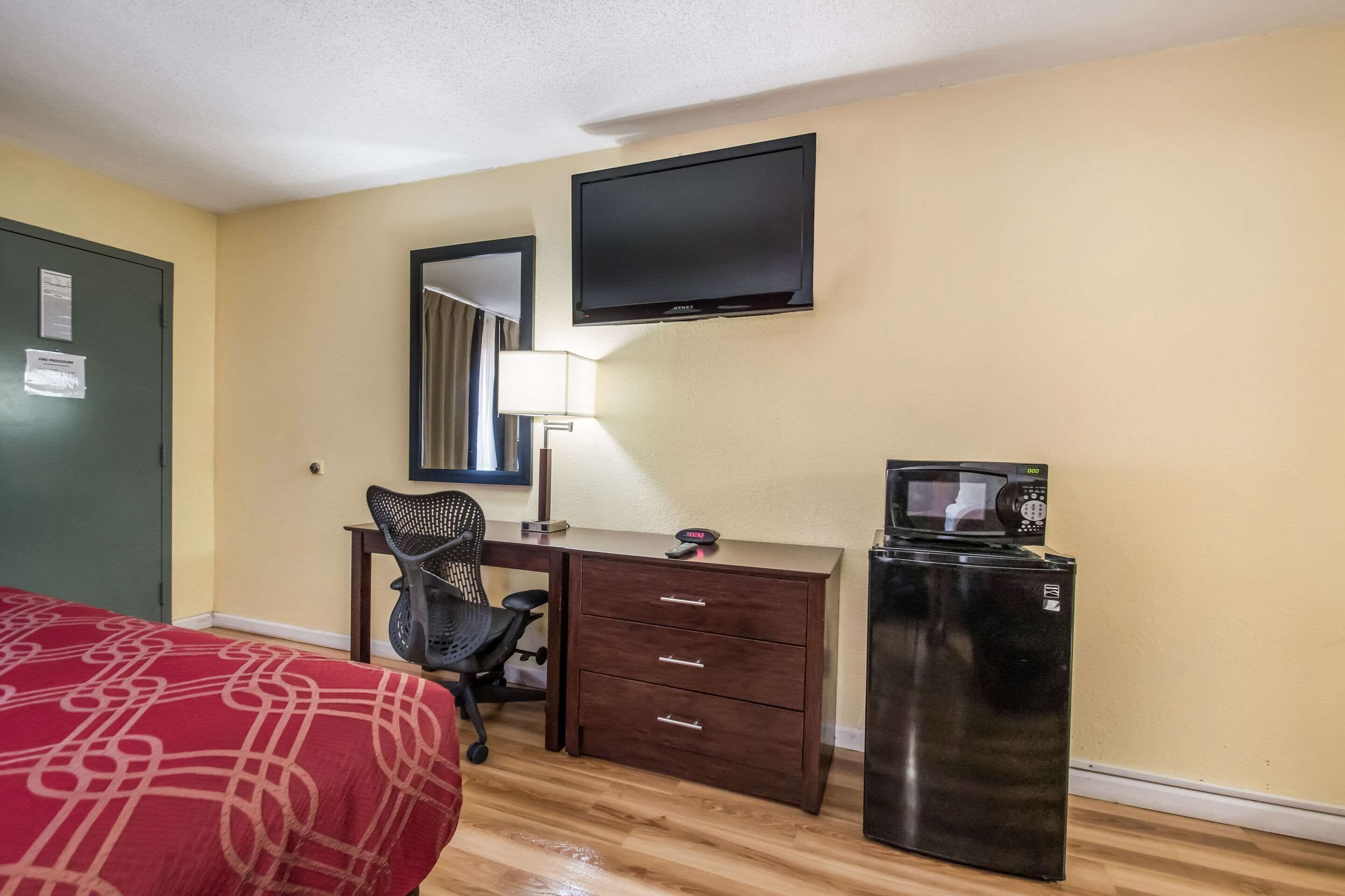 A hotel room with a bed, desk, chair, TV, and refrigerator.